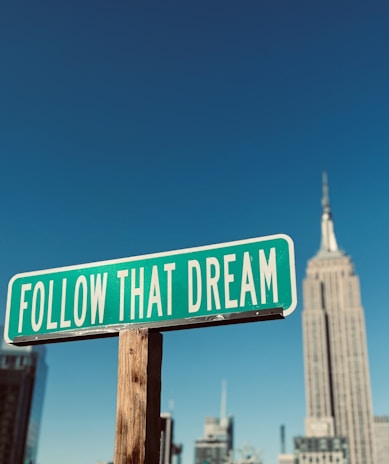 a green and white street sign that says follow that dream