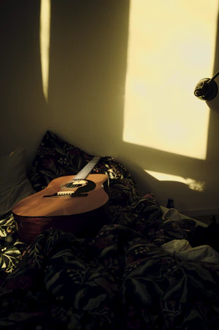 A cozy home setup with an acoustic guitar resting on a wooden chair near a window filled with natural light