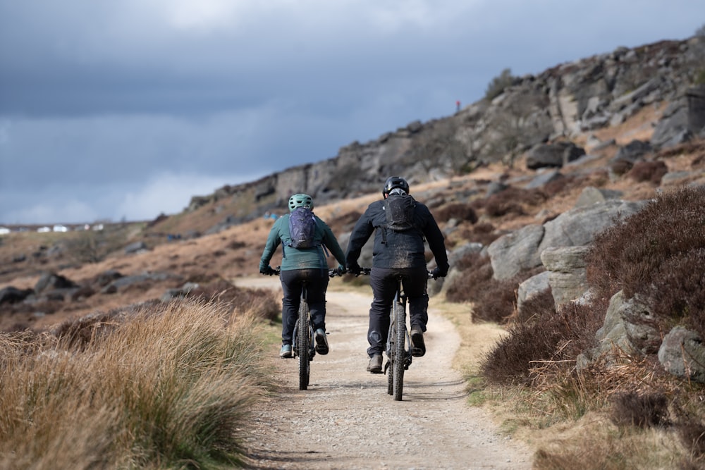 a couple of people riding bikes down a dirt road