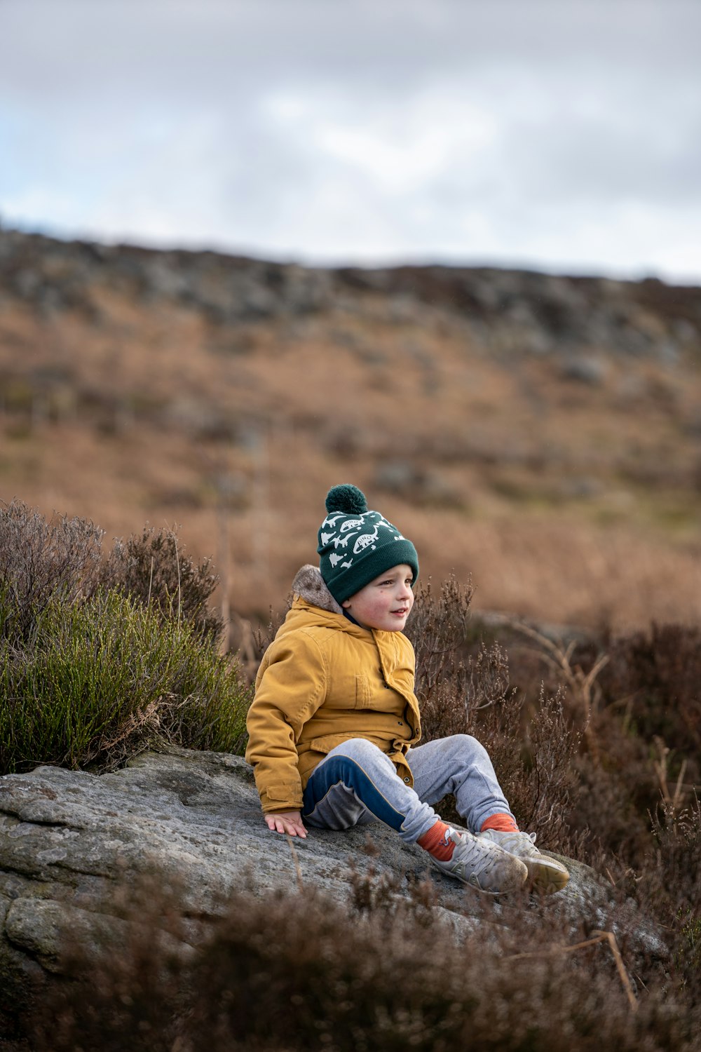 a young boy sitting on top of a rock