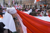 A diverse crowd at a fan zone, many showing off their colorful tatuflags tattoos under bright sunlight.