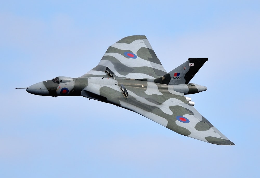 a camouflaged fighter jet flying through a blue sky