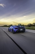A cinematic drone shot of a sleek luxury sports car speeding along a coastal highway at sunset with neon blue highlights.