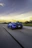 A sleek, high-performance sports car speeding along a coastal highway at sunset, capturing the thrill of automotive passion.
