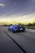 A sleek, high-performance sports car speeding along a coastal highway at sunset, capturing the thrill of automotive passion.