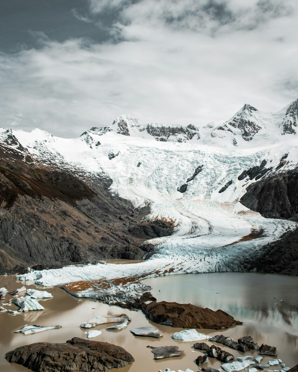 a snowy mountain range with a lake in the foreground