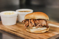 Close-up of a juicy pulled pork sandwich dripping with sauce on a soft bun.