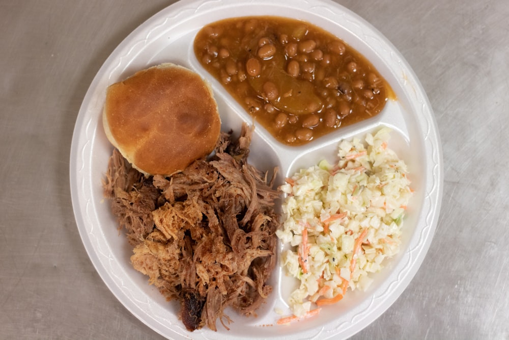 a white plate topped with meat, beans and coleslaw