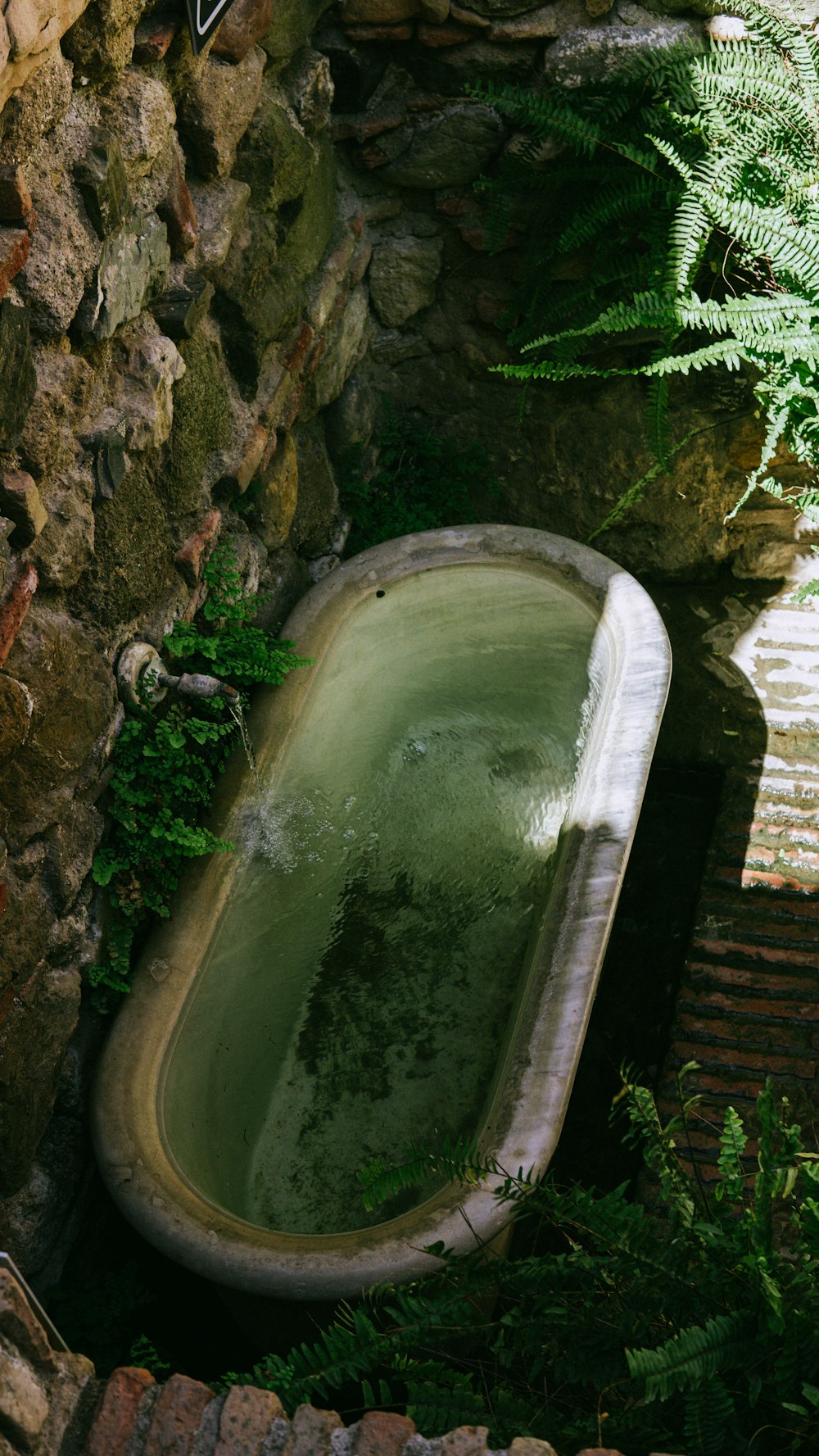 an old bathtub in a stone walled garden
