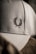 A close-up of a textured fabric cap featuring an embroidered laurel wreath design. The lighting creates a soft shadow effect, highlighting the intricate stitching and the cap's material.