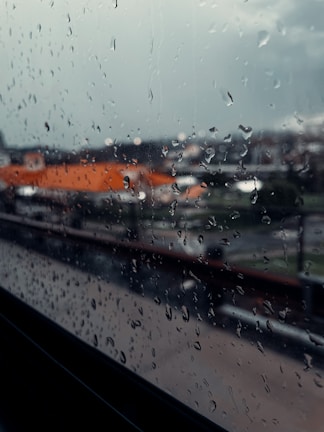 An open window framing a rainy cityscape, droplets blurring the view outside.