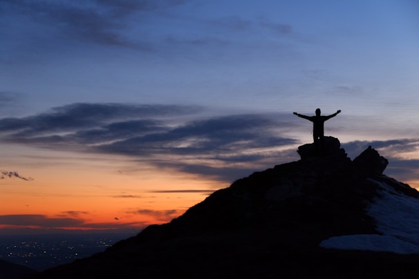 A woman standing confidently on a hilltop at sunset, arms open wide embracing the horizon.