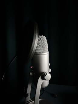 A voice actor performing in front of a microphone with a pop filter and soundproof walls.