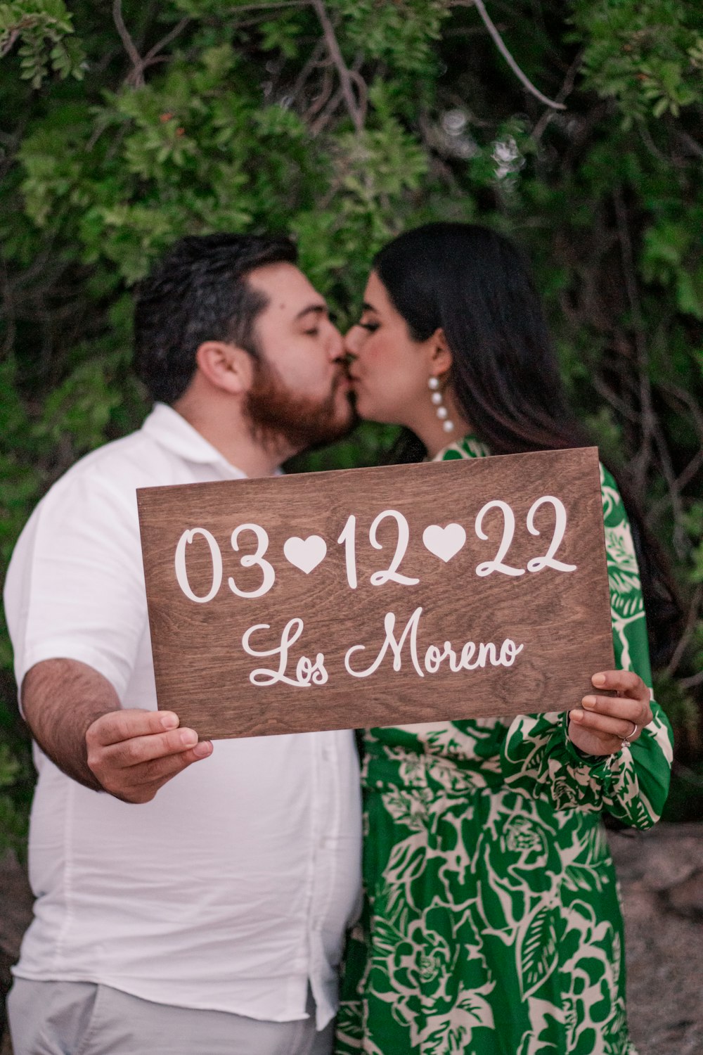 a man and woman kissing while holding a sign