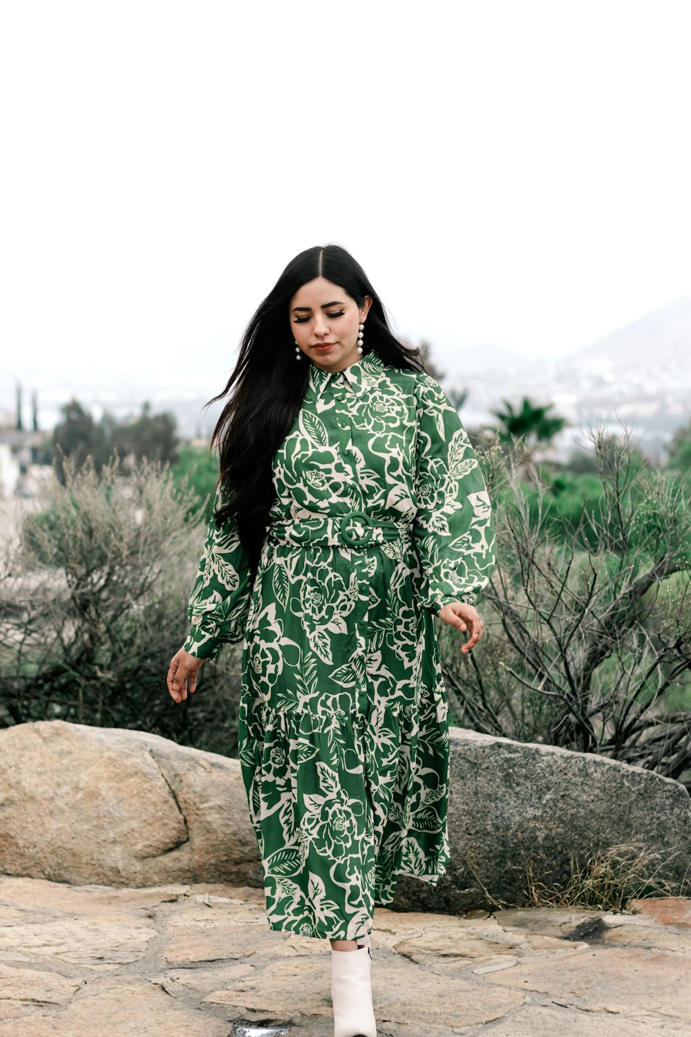 a woman in a green dress is standing on a rock