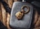 A metallic flask is placed against a backdrop of coiled rope. Resting on the flask is a detailed, gold-colored keychain featuring a lion's head and a circular ring with engraved text. The scene combines rugged textures with sophisticated details, creating a visually intriguing contrast.
