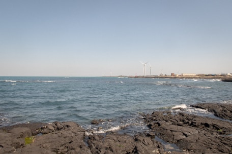 Engineers installing tidal energy equipment along a rocky shoreline under a bright sky.