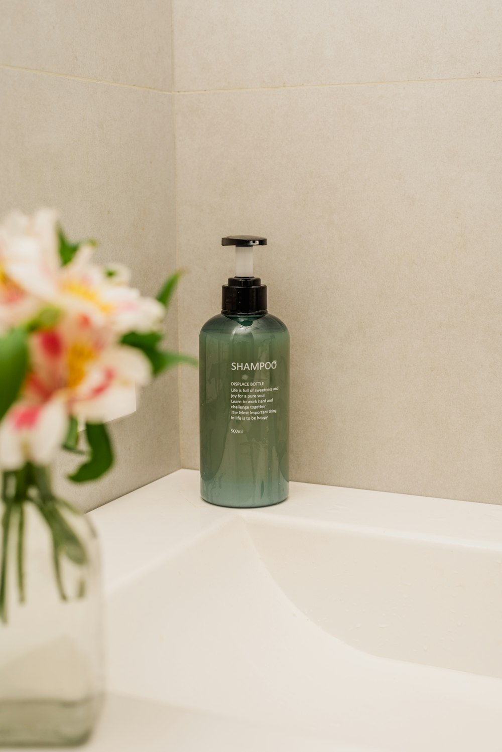 a bottle of shampoo sitting on a sink next to a vase with flowers