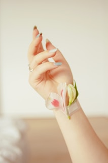 Freshly manicured nails in soft nude tones, holding a delicate pink flower