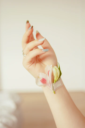 Close-up of a delicate pastel pink manicure with subtle floral nail art on a soft pink background.