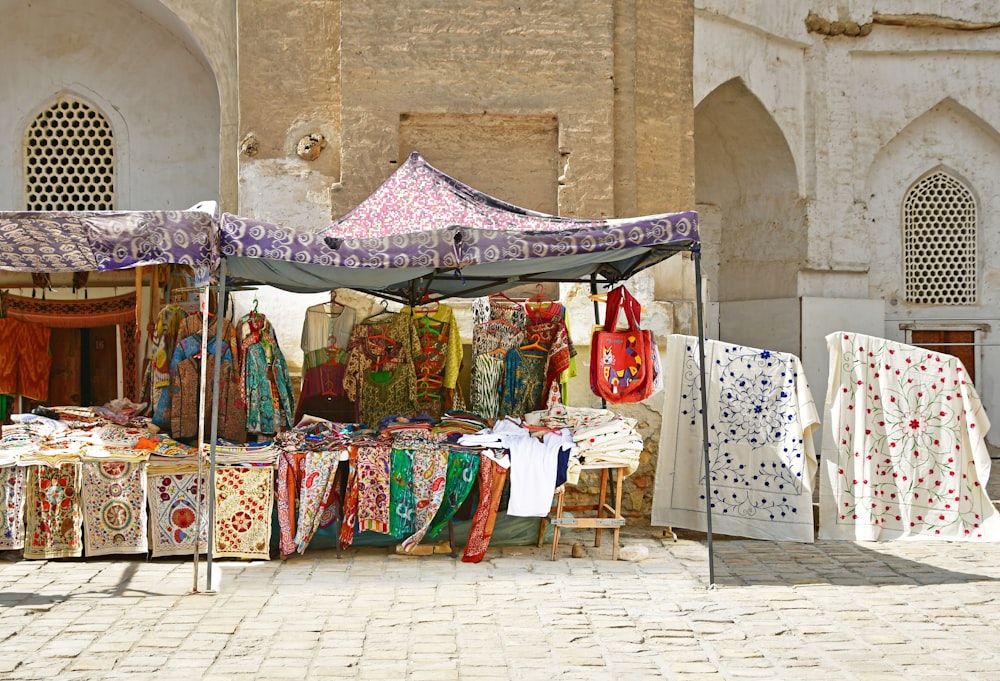 an outdoor market with cloths and umbrellas for sale