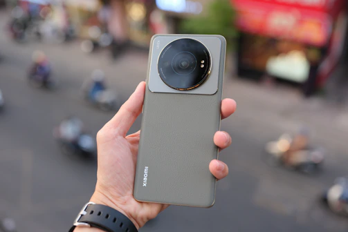 A hand holding a compact phone with a matte finish against a blurred city background.
