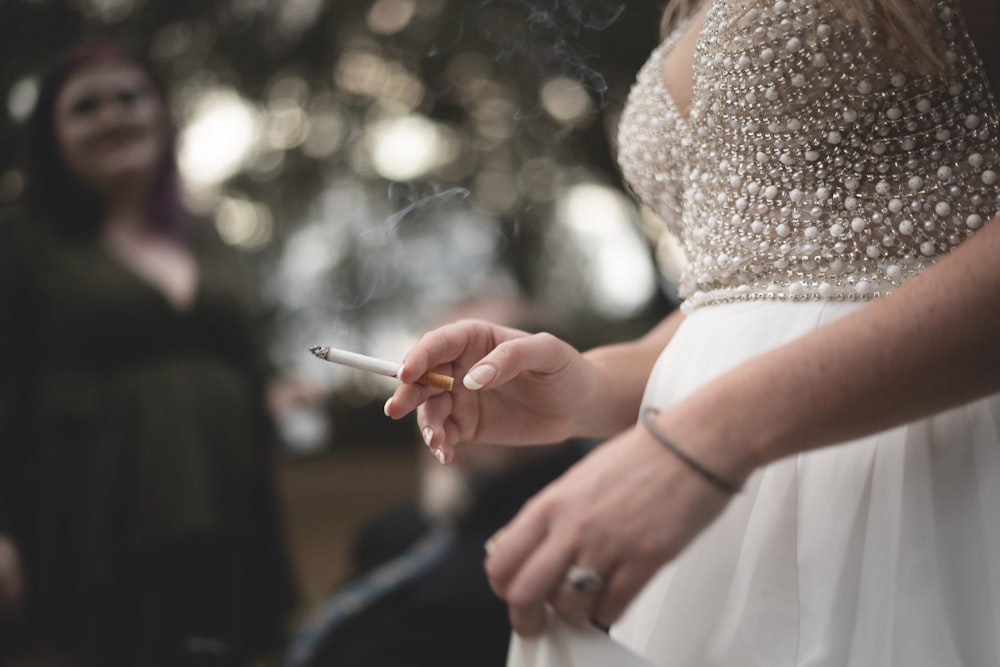 a woman in a white dress holding a cigarette