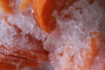 Close-up view of crystalline ice formations surrounding and partially obscuring orange-colored structures, likely frozen food items.