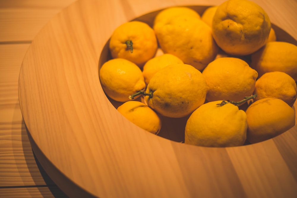 a wooden bowl filled with lemons on top of a table