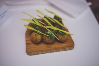 A neatly arranged set of deep-fried balls on a wooden cutting board, garnished with a bright green herb sauce and topped with fresh green leaves.
