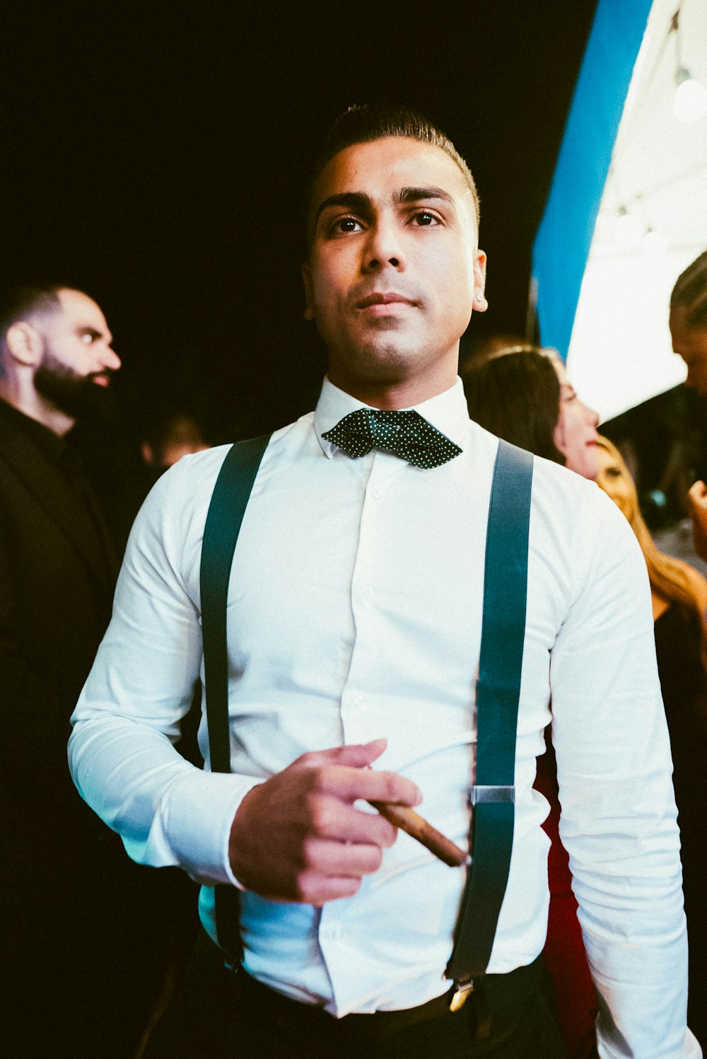 a man in a white shirt and black suspenders smoking a cigarette