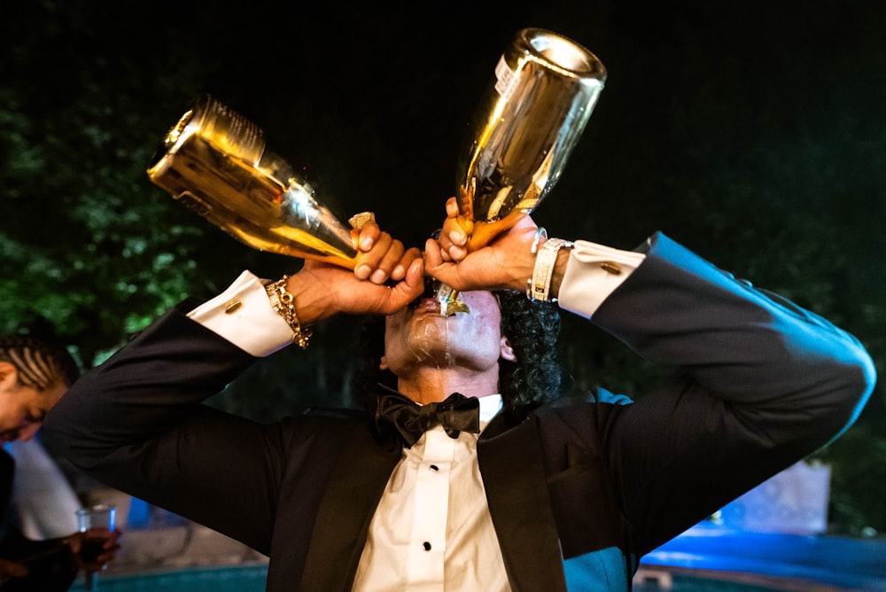 a man in a tuxedo holding two golden cups