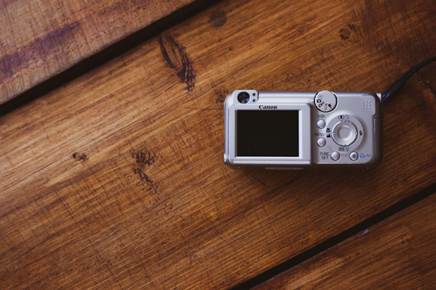 Close-up of a sleek digital camera resting on a wooden table with soft natural light.