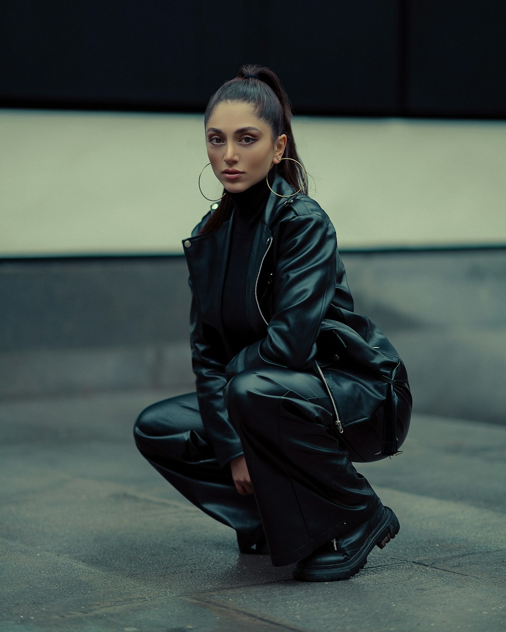 a woman in a black leather outfit crouches on the ground