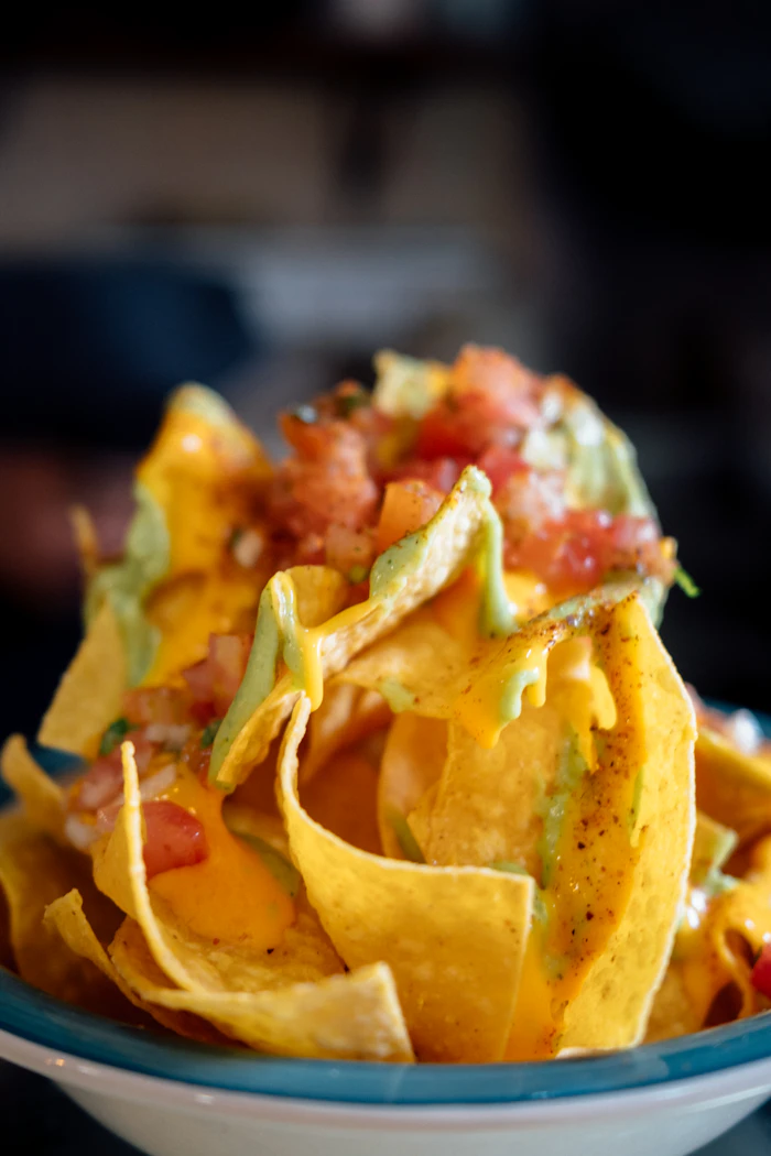 bowl of nachos topped with tomato and avocado