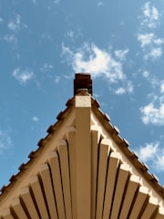 View of a newly framed roof structure with dark timber beams against a cloudy sky.