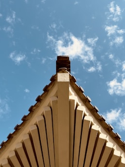View of a newly framed roof structure with dark timber beams against a cloudy sky.