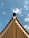 A symmetrical view of a roof's edge with rows of wooden beams extending downwards against a clear blue sky with scattered clouds.