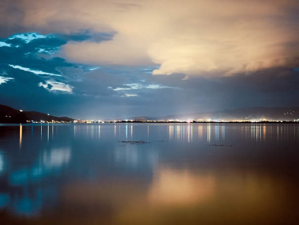 The calm waters of the Tagus reflecting the colorful city lights as night falls over Lisbon.