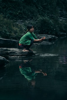 a woman kneeling on a rock in a river