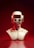 A futuristic sculpture of a humanoid bust with a smooth metallic finish. The head is designed like a retro robot with a rectangular visor and twin circular eyes, set against an intense red gradient background.