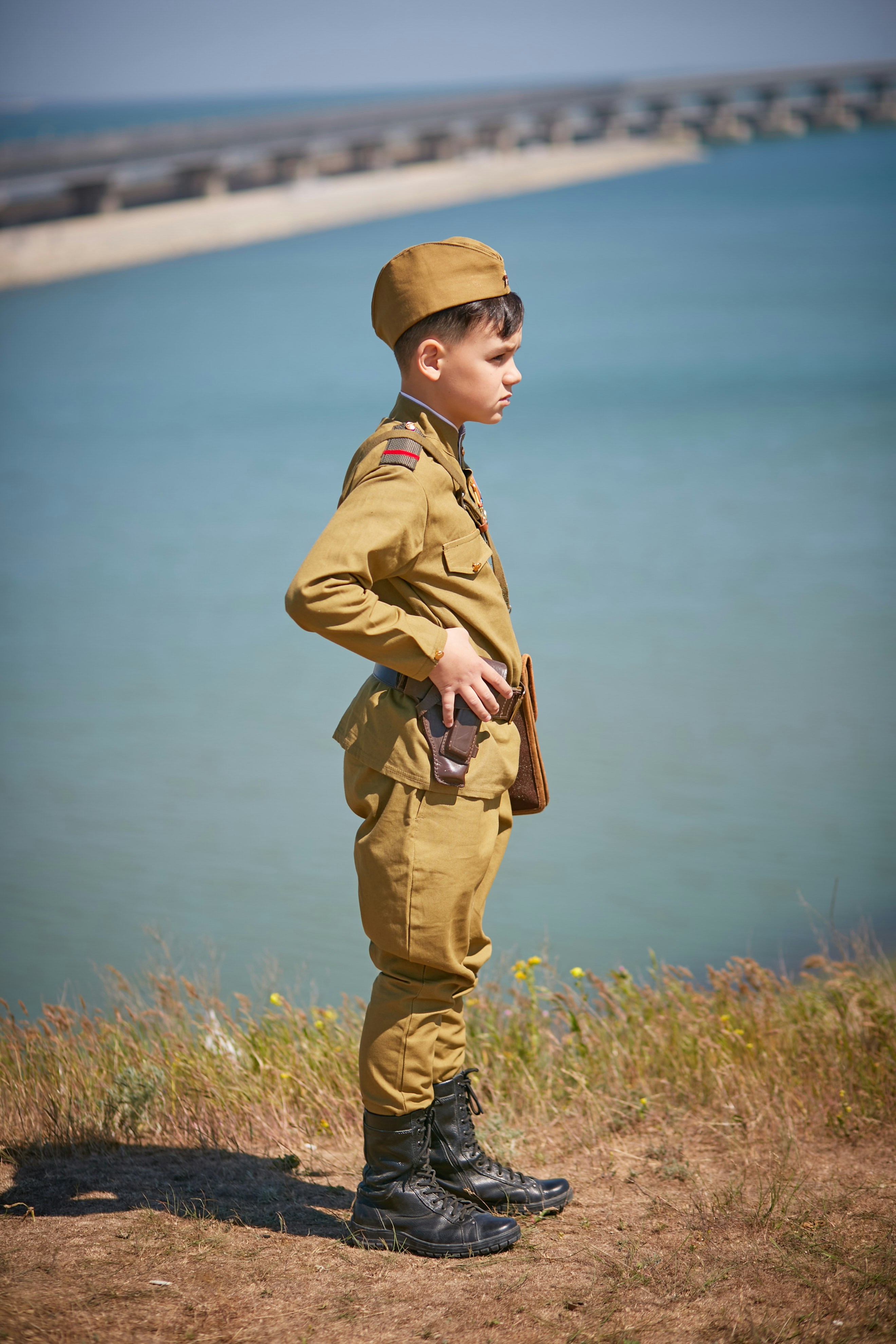 a young boy in a military uniform standing in front of a body of water