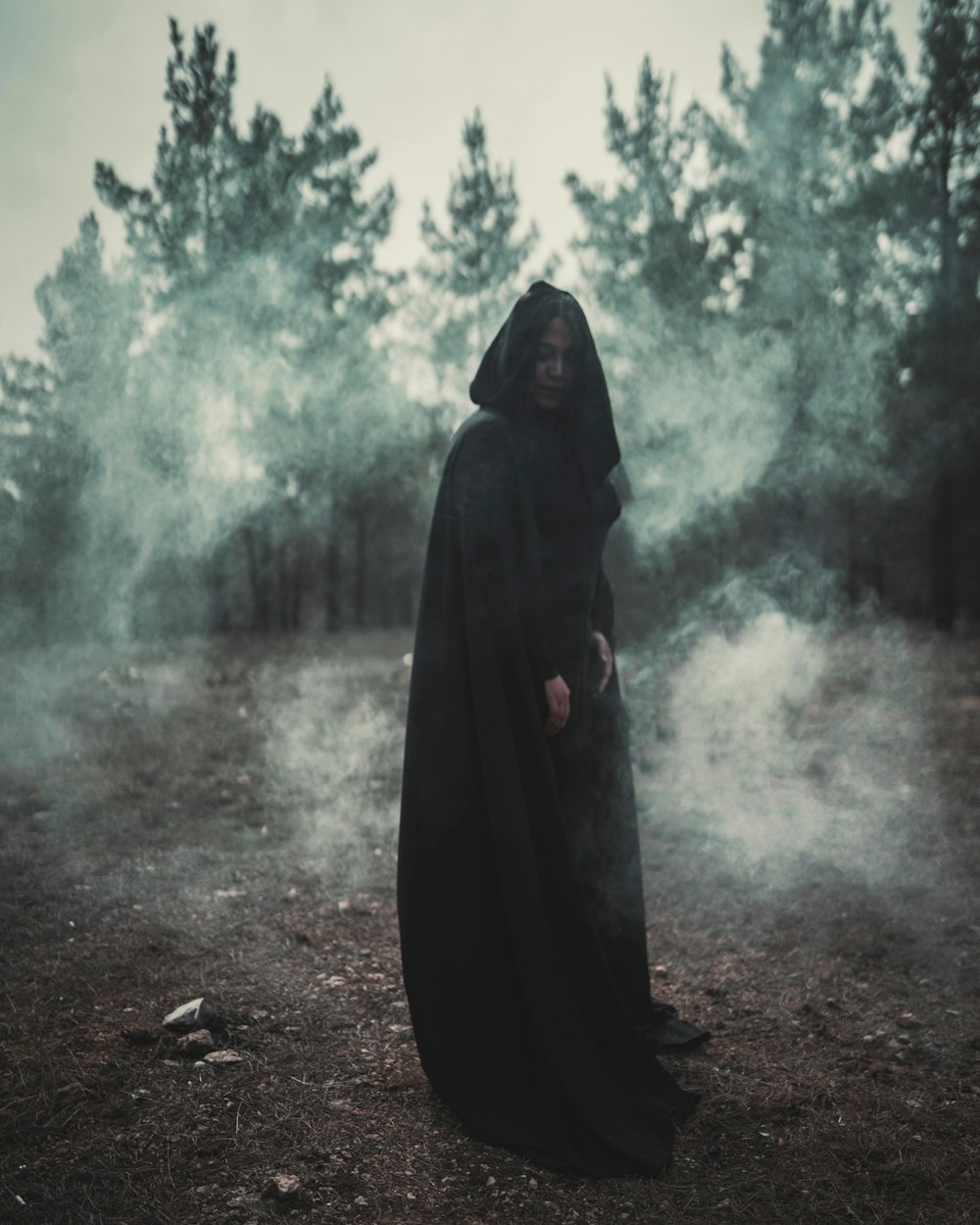 a woman in a black cloak standing in a forest