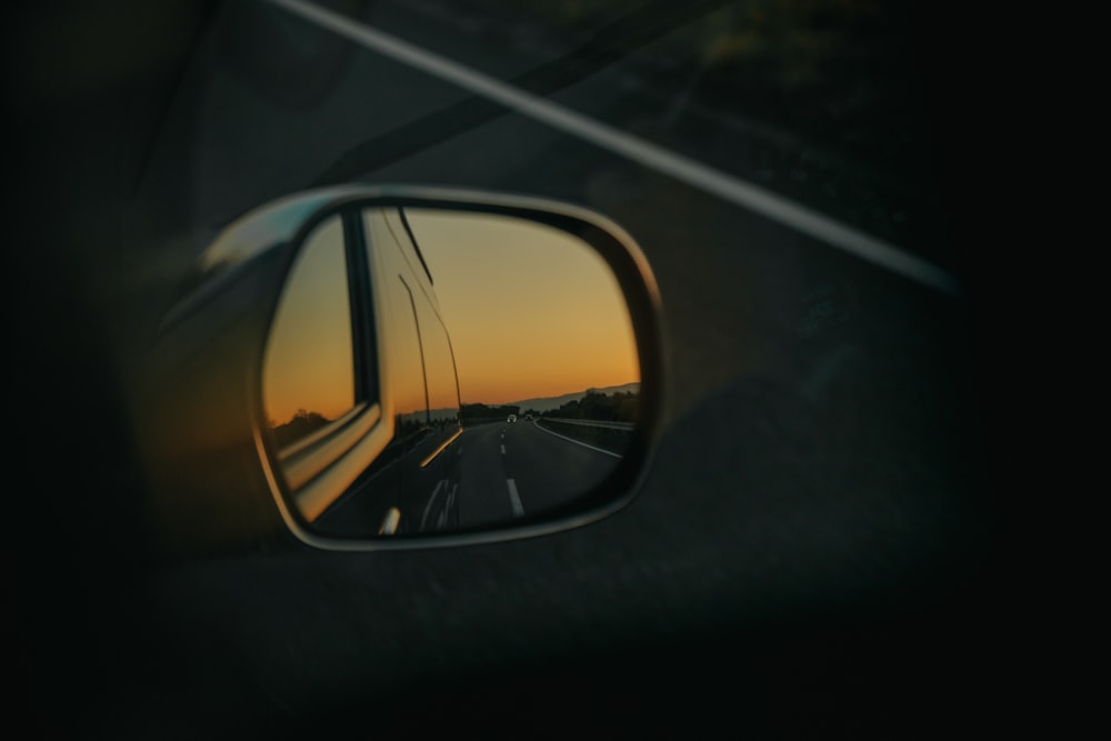 un espejo retrovisor que refleja una puesta de sol en una carretera