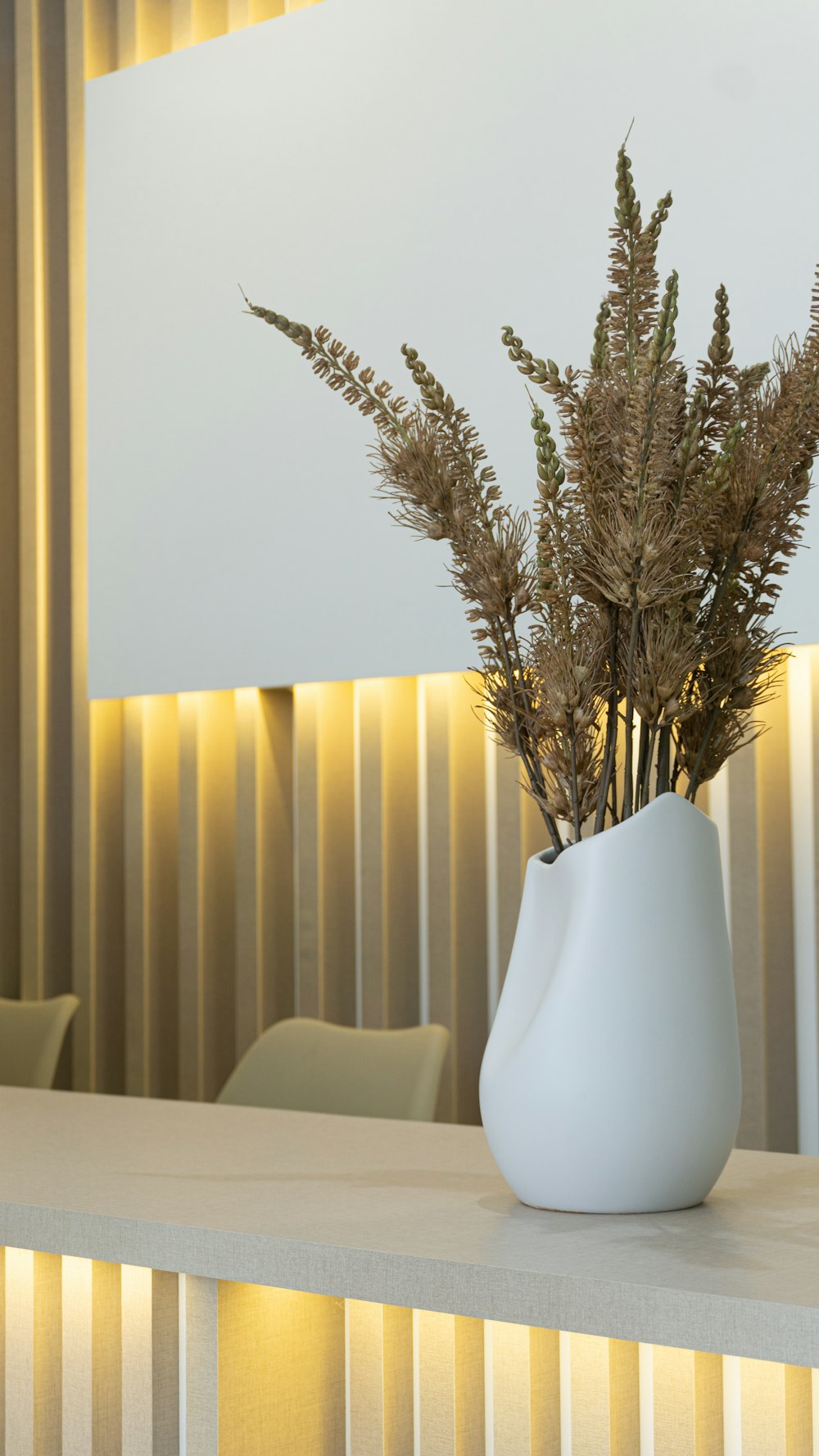 a white vase filled with dried plants on top of a table