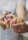 Two hands with wedding rings are joined together, one belongs to a bride in a lace dress holding a bouquet of pink and peach flowers.
