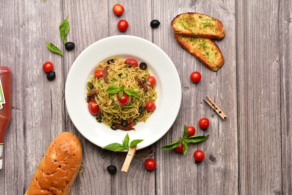 a plate of spaghetti with tomatoes, olives and bread