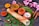 A neatly arranged South Indian meal featuring a dosa placed on a banana leaf, accompanied by three small clay bowls containing sambar, chutney, and yogurt. Surrounding the main setup are various spices, including turmeric and chili powder in small containers, cinnamon sticks, and star anise. Pink flowers add a touch of decoration.
