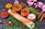 A neatly arranged South Indian meal featuring a dosa placed on a banana leaf, accompanied by three small clay bowls containing sambar, chutney, and yogurt. Surrounding the main setup are various spices, including turmeric and chili powder in small containers, cinnamon sticks, and star anise. Pink flowers add a touch of decoration.