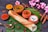 A neatly arranged South Indian meal featuring a dosa placed on a banana leaf, accompanied by three small clay bowls containing sambar, chutney, and yogurt. Surrounding the main setup are various spices, including turmeric and chili powder in small containers, cinnamon sticks, and star anise. Pink flowers add a touch of decoration.
